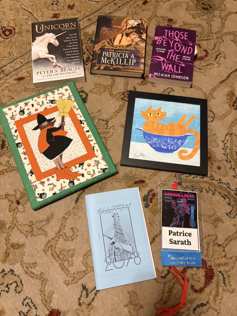 books and art laid out on a rug, along with a badge from ArmadilloCon.